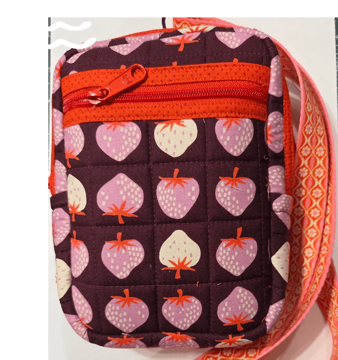 A small crossbody bag with a strawberry pattern and orange accents.
