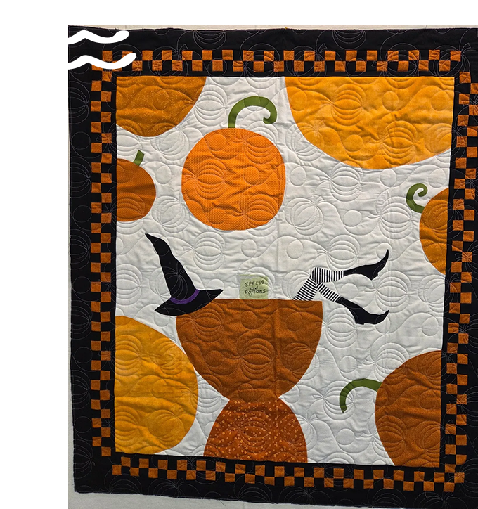 A Halloween-themed quilt with pumpkins, bats, and a cauldron design.